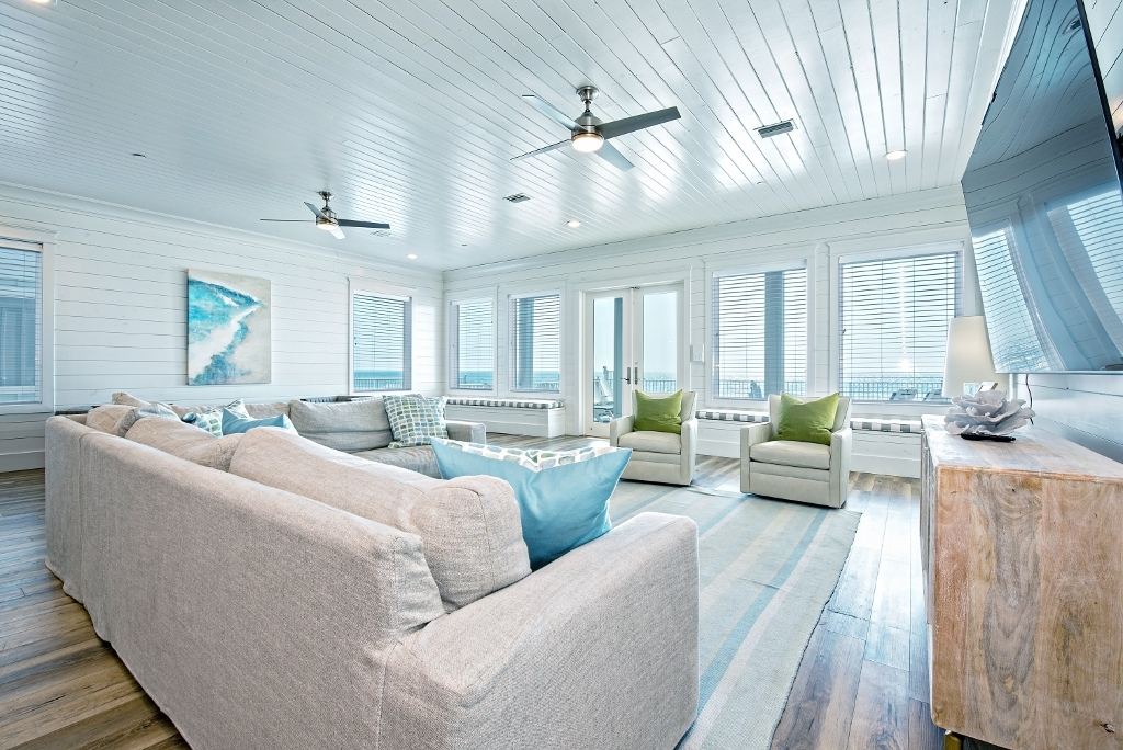 Beach house living room with sectional sofa, ceiling fans and windows facing the water