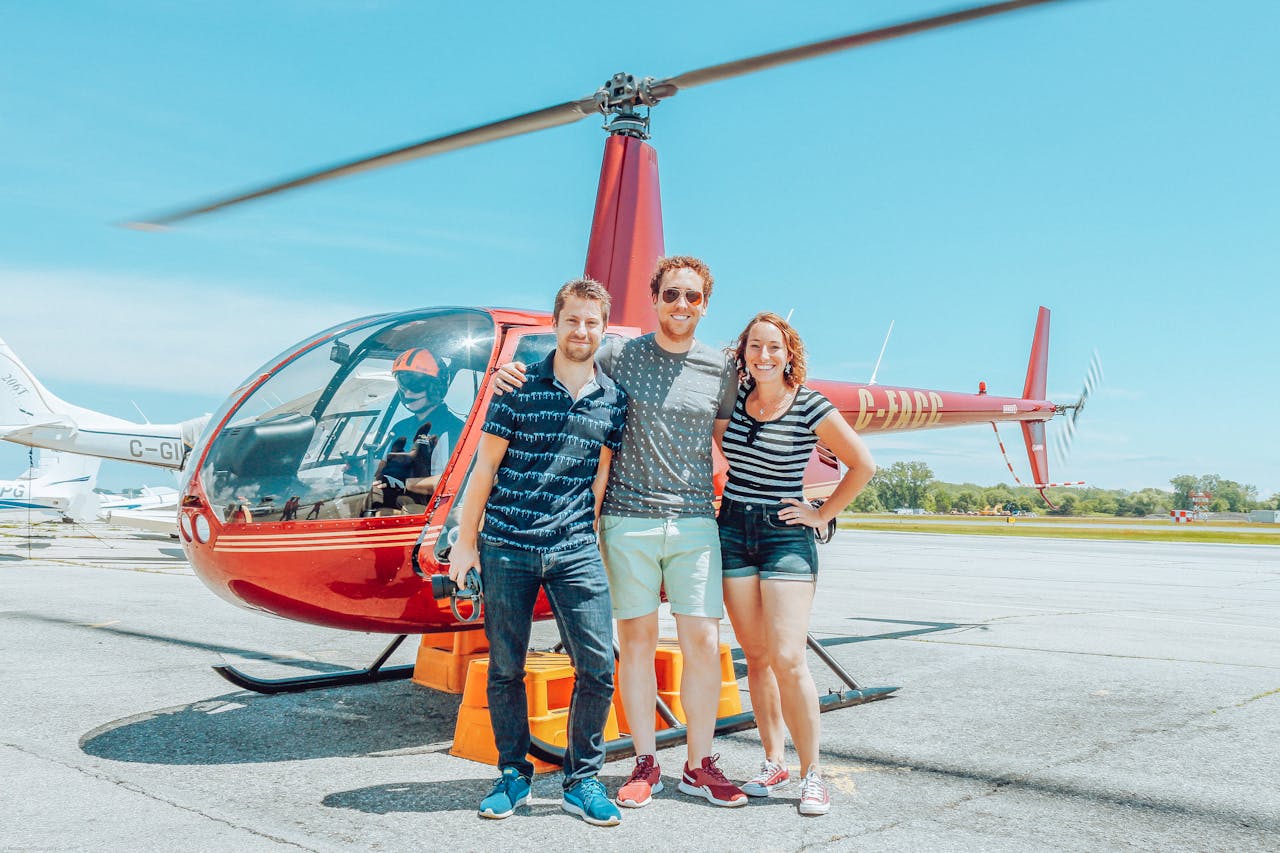 Three people standing in front of a red helicopter on an airfield before a helicopter tour
