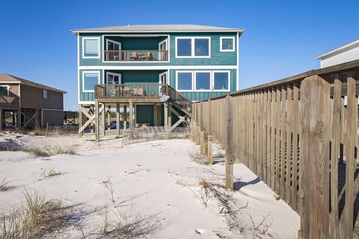 Teal beach house beside a wooden fence at Pier Serenity in Fort Morgan, Alabama